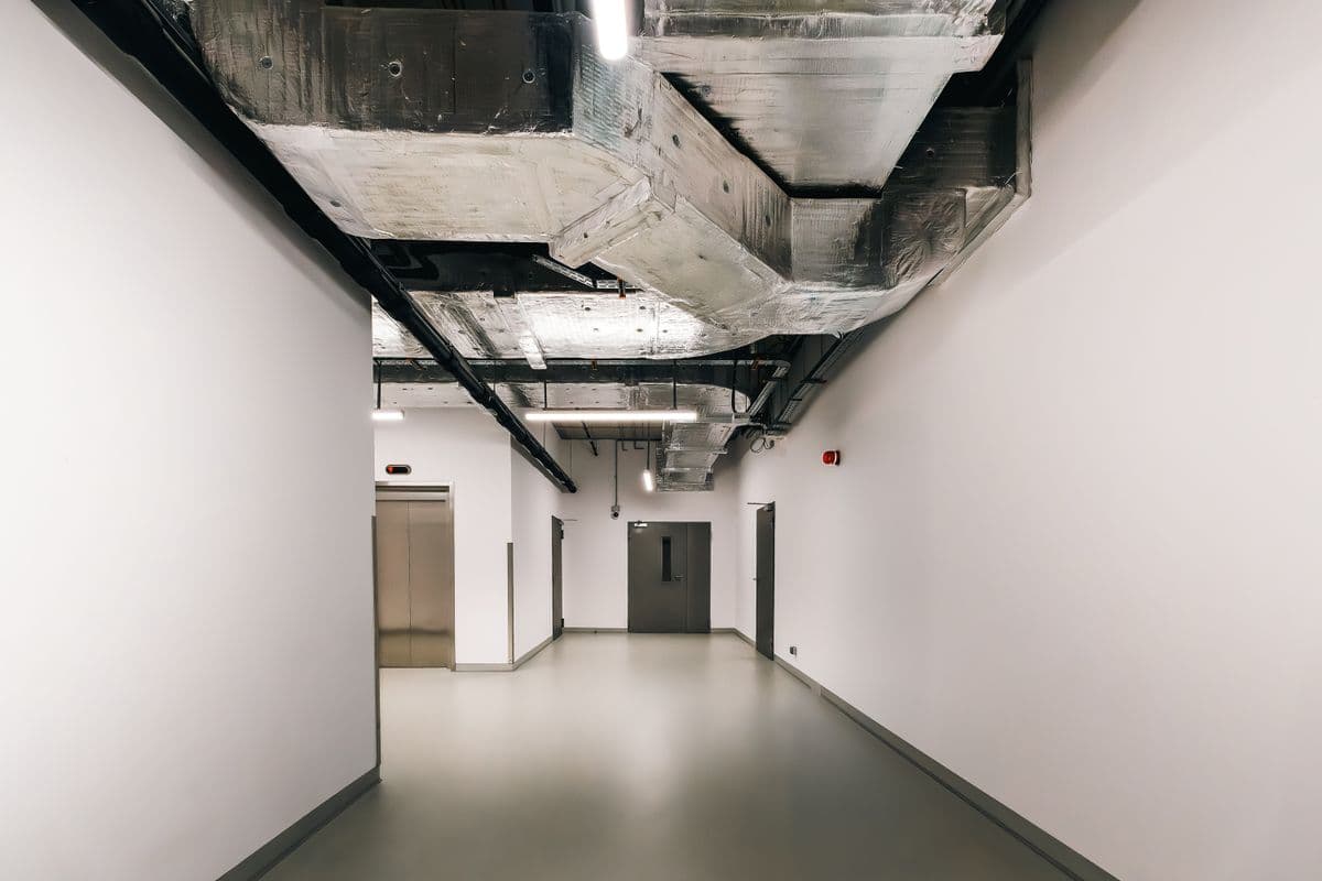 Industrial building corridor with exposed HVAC ductwork and insulated ventilation systems overhead