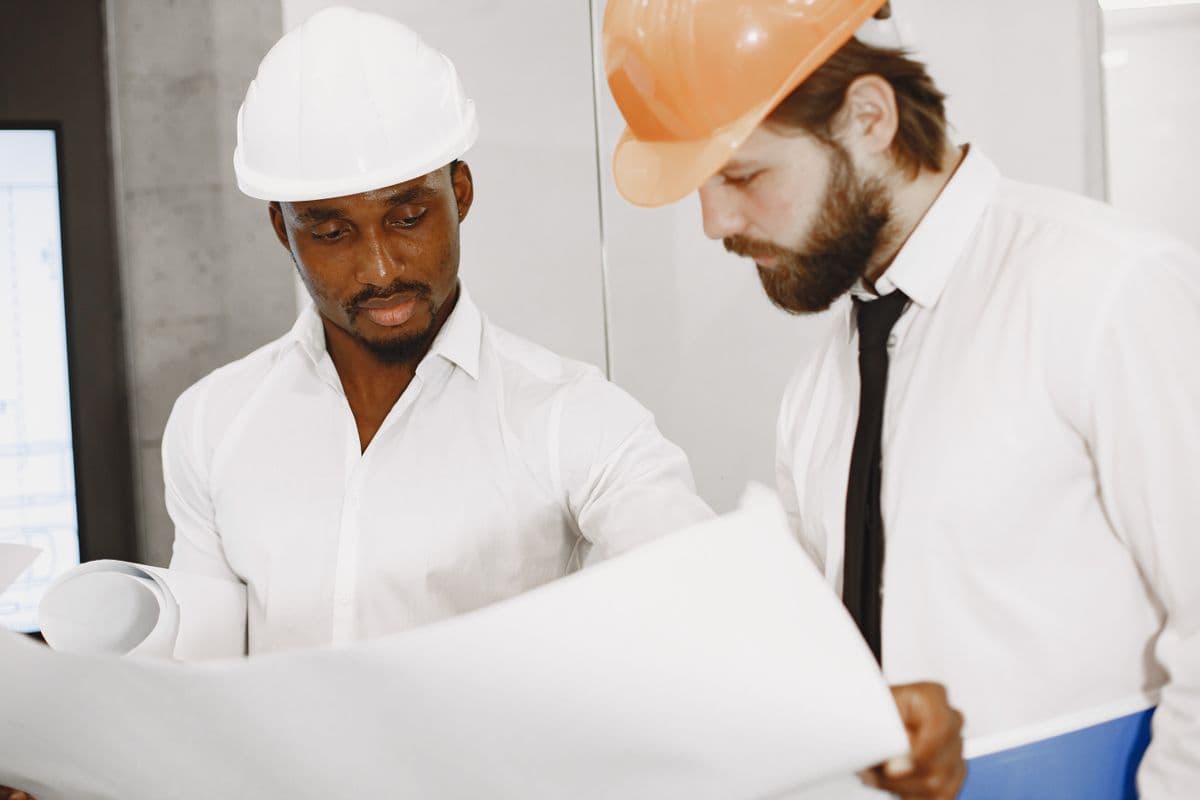 Two engineers in hard hats reviewing detailed construction blueprints indoors