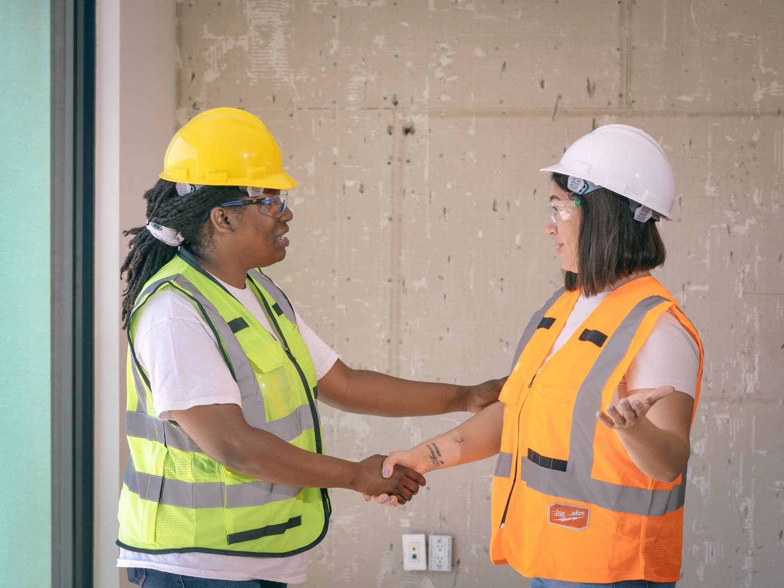 Two construction partners in hard hats shaking hands on a job site
